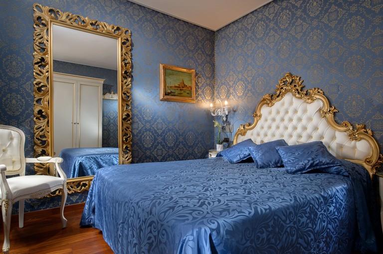 A bed with blue silk bedspread and gilded furnishings in an elegant hotel room at Hotel Santa Marina