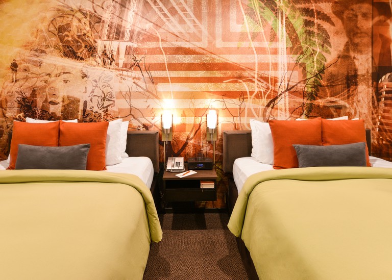 A colorful room at the Tangerine, with two twin beds with orange pillows against an orange wall with printed wall art