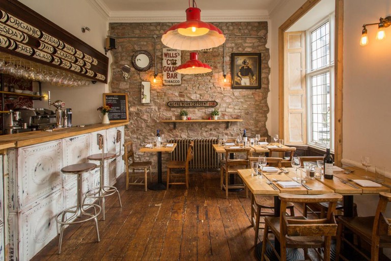 Quaint restaurant space at the Rodney Hotel in Clifton, Bristol, with exposed stone wall and rustic wood furnishings and floors