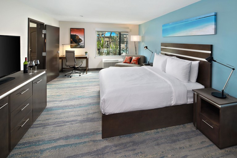 Spacious bedroom with dark wood furnishings and pops of blue at the Cove Hotel, Ascend Hotel Collection in Long Beach