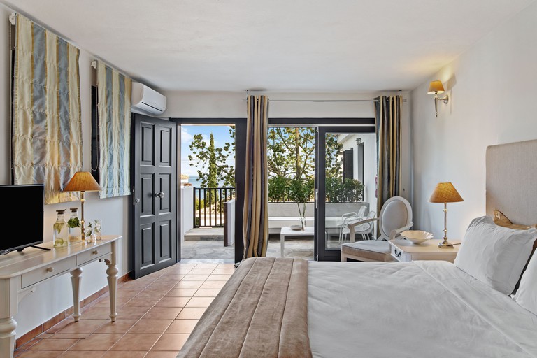 Double bed on tiled floor in room with chair, TV and air conditioning, plus a private seated terrace at Aegean Suites Hotel