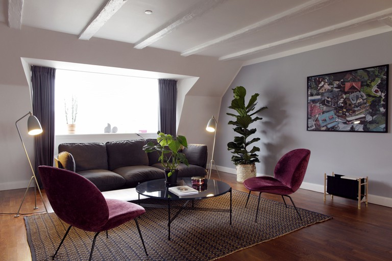 Stylish living room with brown couch, retro plum velvet chairs, potted plants and photo wall art at Arthur Aparts Copenhagen