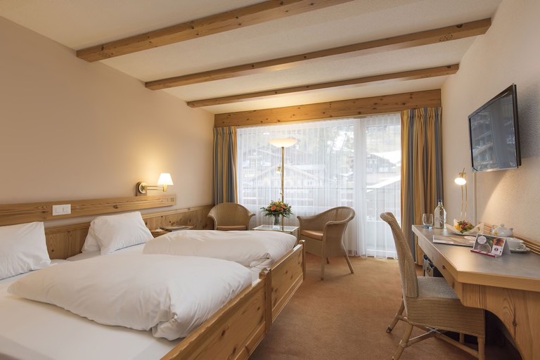 Cosy double room with exposed-beam ceilings, rustic wood furnishings and tan carpet at Sunstar Hotel Grindelwald
