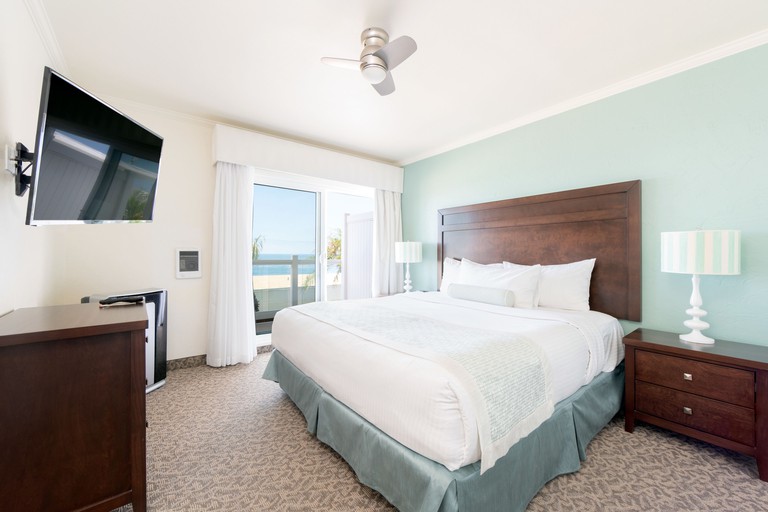 Double bed facing wall-mounted TV in neutral-toned room with overhead fan at Capri Laguna on the Beach