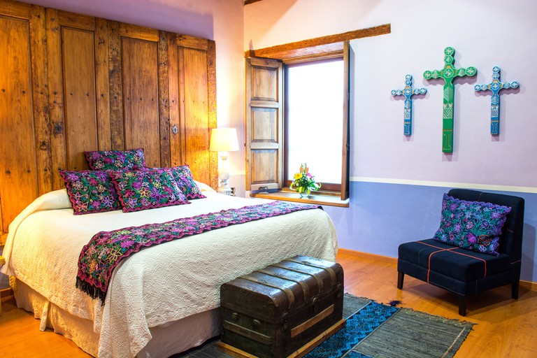 Cosy bedroom with colorful traditional Mexican embroidery and crosses, antique chest and rustic wood accents at Casa Santa Lucia