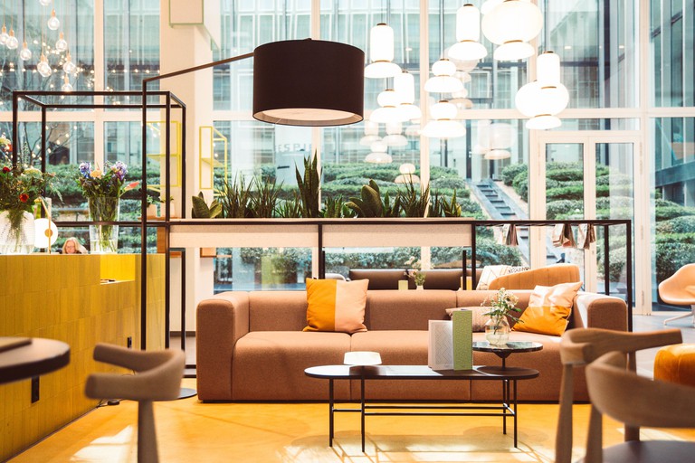A lounge area with soft furnishings, hanging lights and lots of greenery at Hotel Casa Amsterdam