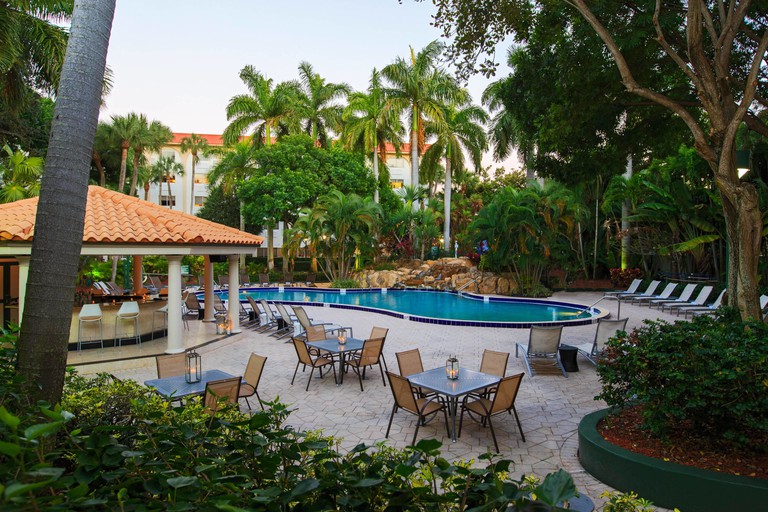 Tropical outdoor pool area with covered bar, dining tables and lounge chairs at Renaissance Boca Raton Hotel