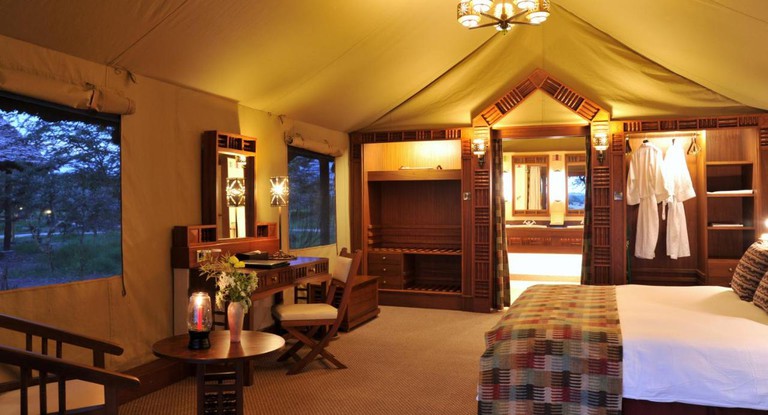 A large bed and carved wooden furniture and decor in a large tent at Sweetwaters Serena Camp