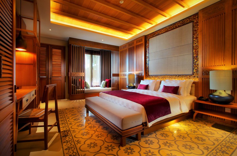 Dark wood panelling, a bed, desk and window seat in a hotel room at the Haven Suites Bali Berawa