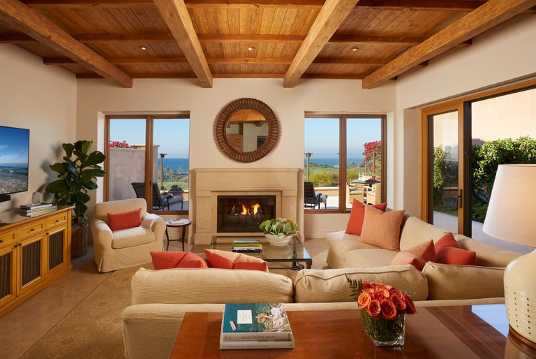 Long cream corner sofa and armchair, flat-screen TV and fireplace in wood-beamed living area at the Resort at Pelican Hill