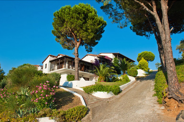 Hillside exterior of white-painted Villa Anna Maria, with verdant greenery, trees and a sloping road by its side