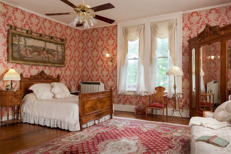 A classically styled guest room at Vrooman Mansion, with beautiful period wooden furniture, bold wallpaper and a plush rug