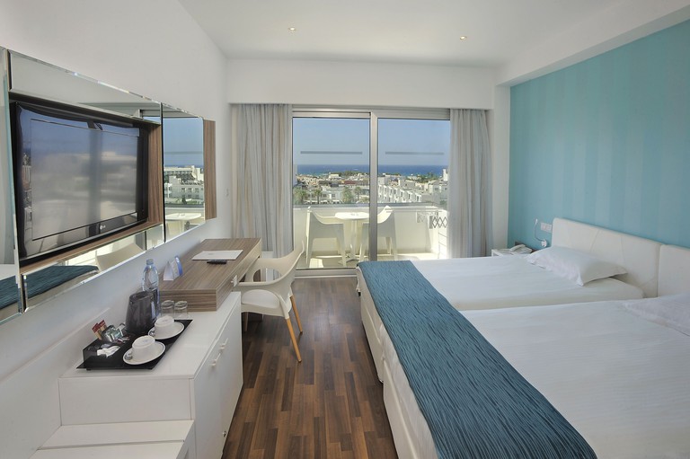 Two single beds in simple room with balcony overlooking town and ocean at Nestor Hotel