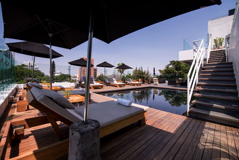 Sun loungers under parasols are arranged around the pool on the roof deck at Hotel Demetria.