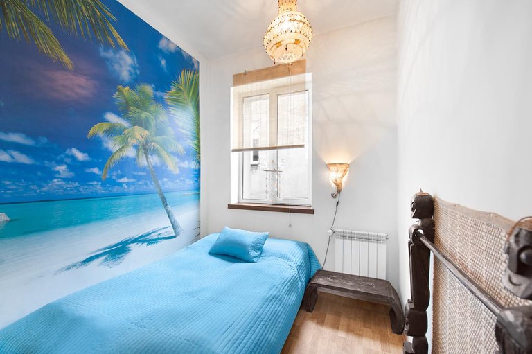 A bed with blue bedding and art of a beach with palm trees in a guest room at Mundo Hostel