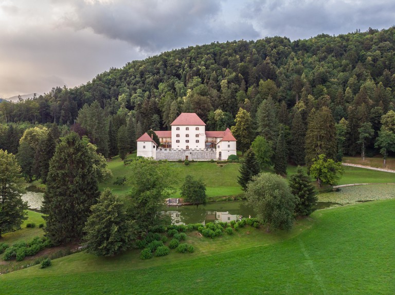 Strmol Castle with tree-covered hills in the background and lawn and a river in the foreground