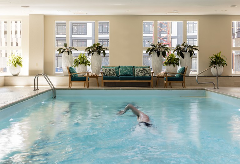 A person doing laps in the indoor pool at Seaport Hotel, with cushy patio furniture and potted plants in the background