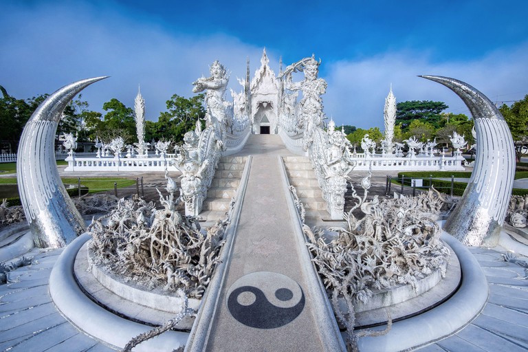 Path leading to the White Temple, also known as Wat Rong Khun, in Chiang Rai, with a ying and yang symbol and intricate stone sculptures