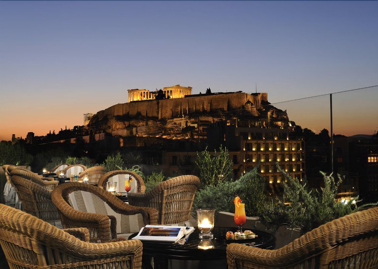 Outside dining at the Royal Olympic Hotel with a view of the Acropolis in the skyline a cocktail on the table