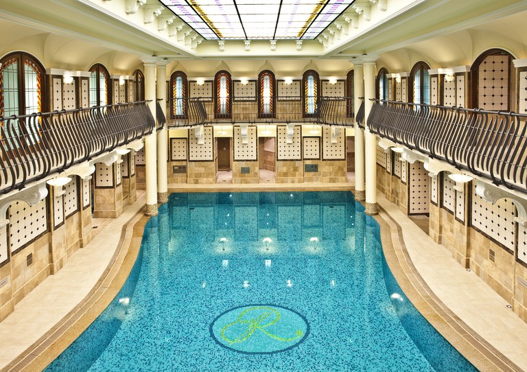The blue-tiled indoor swimming pool at Corinthia Budapest, with wrought-iron railings around the second floor