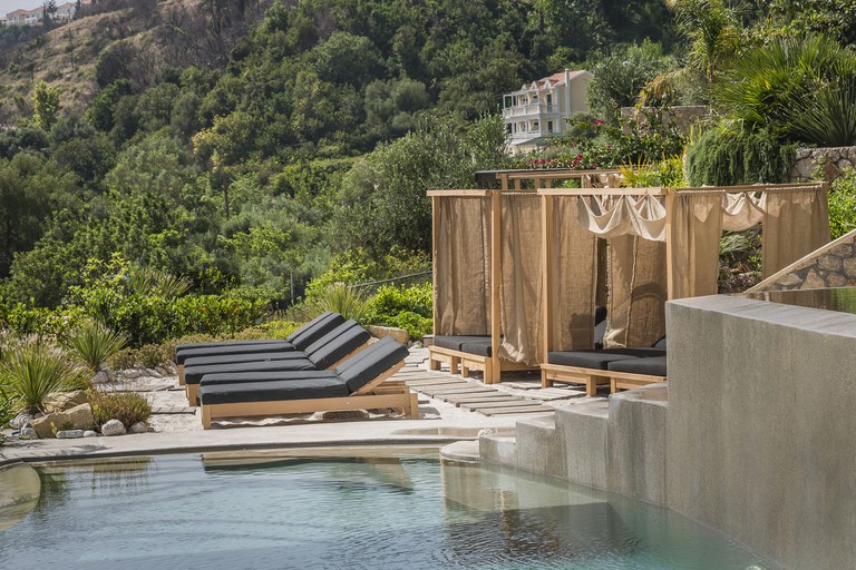 Sun loungers beside an outdoor pool at F Zeen Retreat, with a view of a large green hill