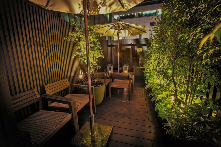 An outdoor seating area at Glansit Kyoto Kawaramachi, with lights, plants, wooden chairs, tables, candles and parasols