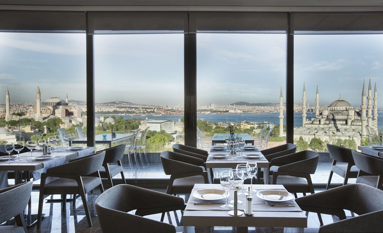 Tables set for dining in the restaurant of Hotel Arcadia Blue, with a view from the floor-to-ceiling windows of the Hagia Sophia, the Blue Mosque and the Bosphorus