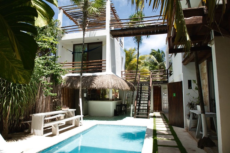 Small pool in courtyard with palapa-shaded bar under white buildings with log-built stairs and railings at Residencia Gorila