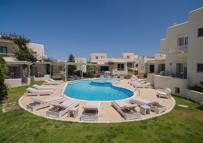 The communal pool at the Illiada Villas is surrounded by sun loungers, grass and classic Greek holiday villas.