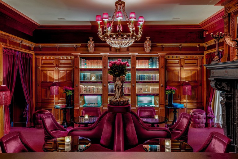 The sitting area with plush pink velvet chairs, wood panelling, a wood bookcase and a chandelier at Maison Souquet