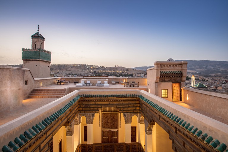 A rooftop seating area overlooking Fes at sunset, with a view to a Moroccan-style courtyard below the roof at Dar Bensouda