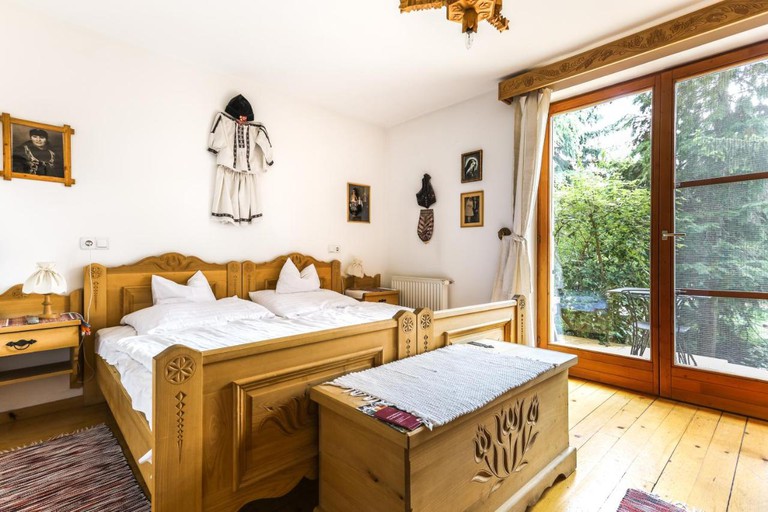 Twin beds in carved wooden frames in an airy, rustic room with traditional Hungarian art and artefacts on the wall at Bagolyvar.