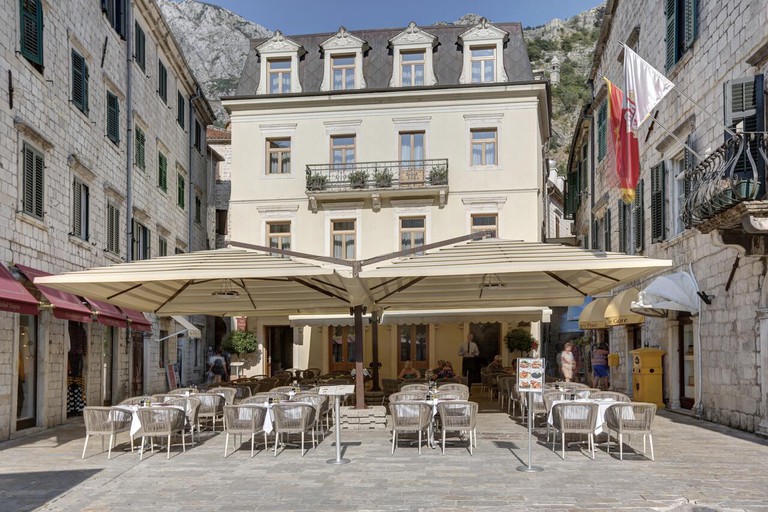 Seating underneath large umbrellas at the front of Hotel Vardar, surrounded by pretty stone buildings in Kotor