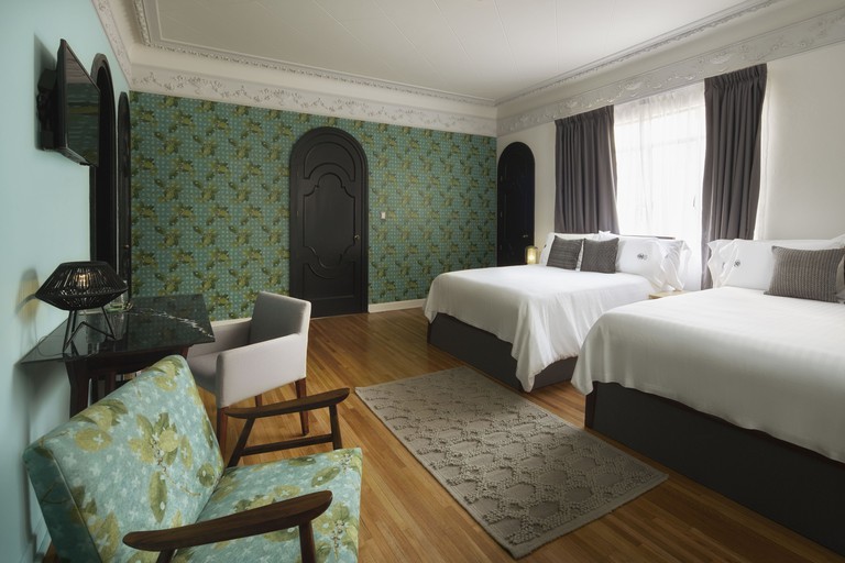 Double beds in large room with lemon print wallpaper, large window and black doors with rounded frames at Pug Seal.