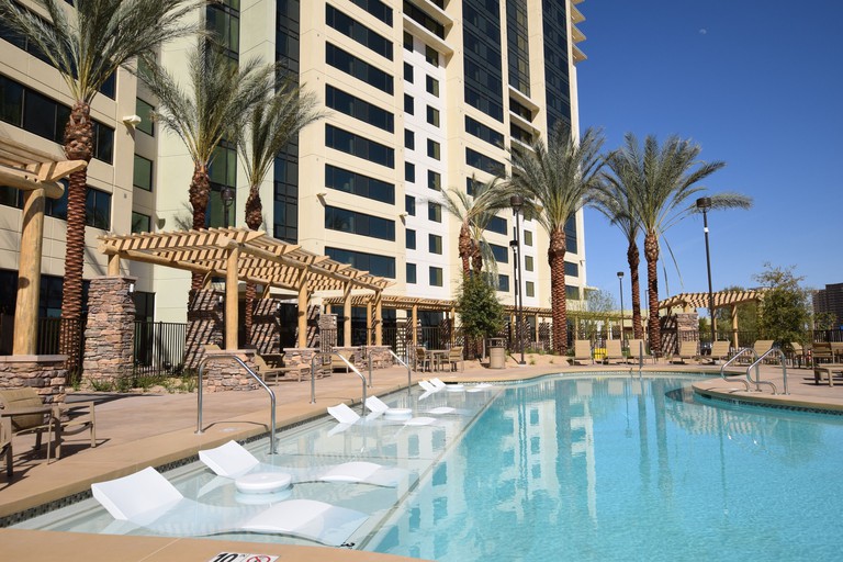 In pool loungers and palm trees surround a pool next to a high-rise building in Las Vegas.