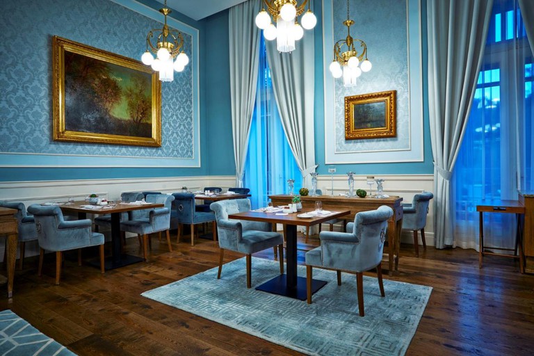 The plush dining room, with blue velvet chairs and carpets and grand windows, at the Hotel Lomnica in the High Tatras Mountains in Slovakia