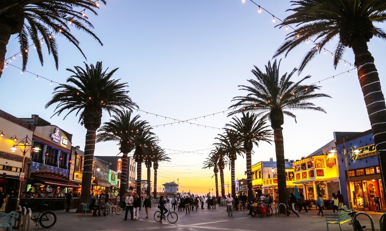 Large pedestrian area by the pier in Hermosa Beach, with bars lining the street on either side and string lights strewn across the palms
