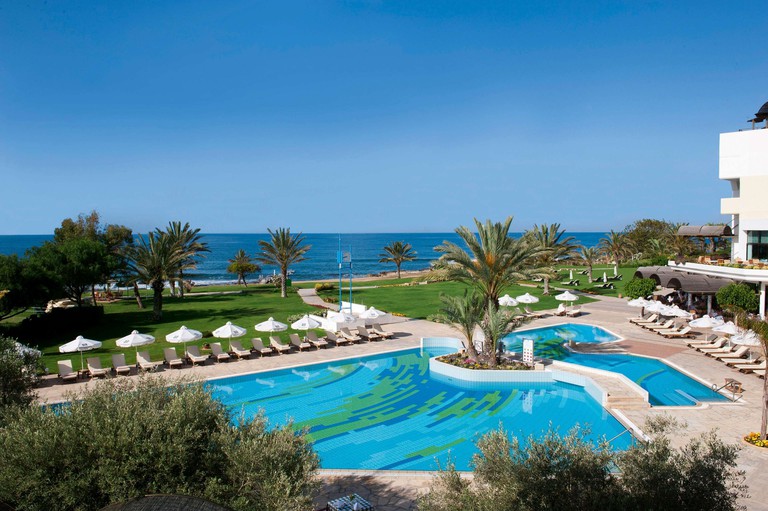 Large outdoor swimming pool area with loungers next to beach at Athena Royal Beach Hotel in Paphos, Cyprus