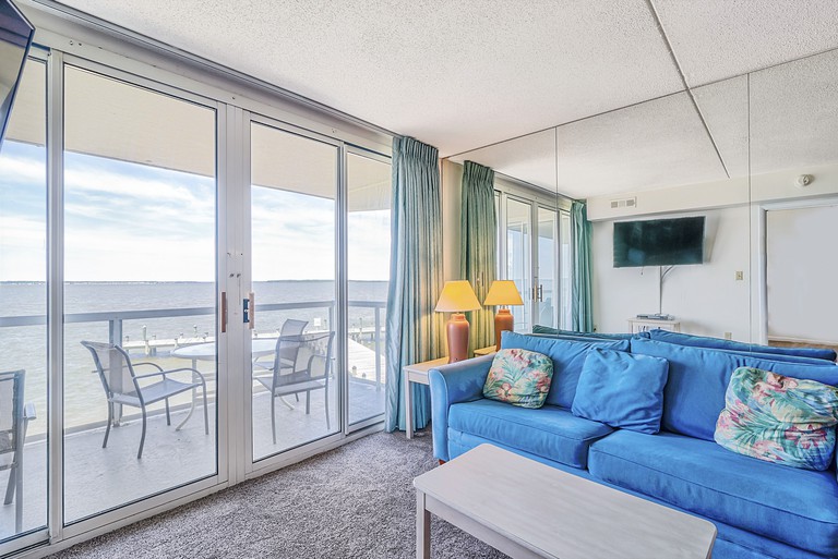 A room at the Bay Club Resort, with a mirrored wall, a blue sofa and a balcony with sea views