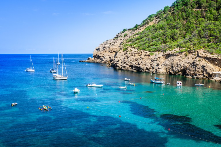 The sheltered cove of Cala Benirrás is surrounded by protective rocky shores and a scattering of sailing boats are moored in its beautiful waters.