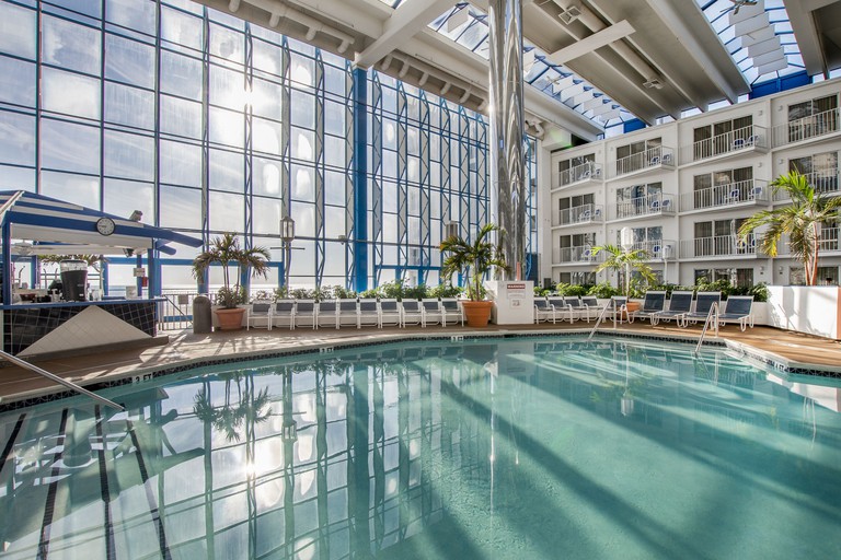 The indoor pool in a four-storey atrium at Princess Royale Oceanfront Hotel & Resort, with chairs, a bar and balconied rooms