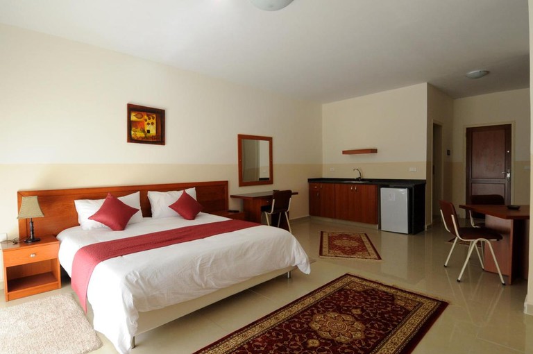 Plain guest room at Byblos Guest House, with light painted walls, tiled floor, a large bed, some desks and two chairs