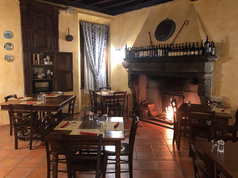 Wooden tables inside Antica Trattoria del Risorgimento restaurant, with a fire blazing in the fireplace