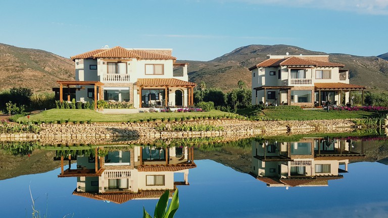 Beautiful view of two white villas at the El Cielo Winery & Resort, with a lake-front location and a mountain backdrop.