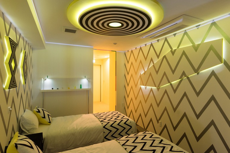 Two single beds in Artist Hotel BnA Hotel Koenji with zig-zag wallpaper and matching bedding, with fluorescent lights