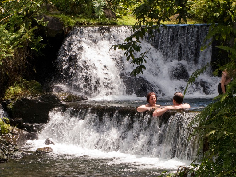 AT3Y1X Costa Rica La Fortuna Tabacon Hot Springs resort guests sitting in pool between thermally heated waterfalls