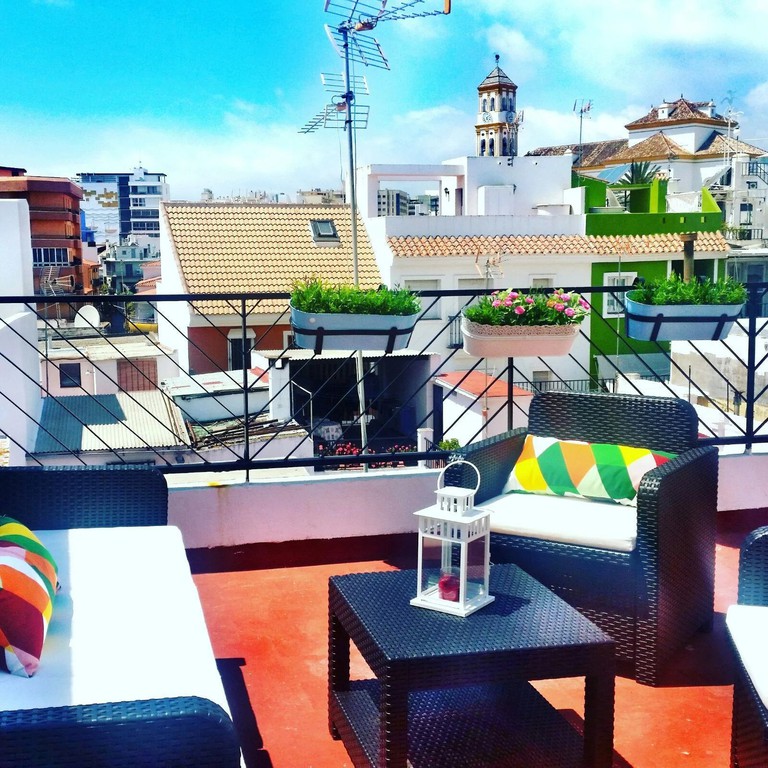 A rooftop seating area at Hostal Berlin, with table and chairs, colourful pillows and a terracotta-coloured floor