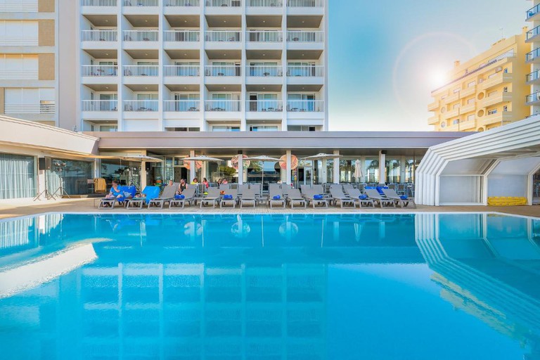 A sunny outdoor swimming pool at Jupiter Algarve Hotel, with sun loungers and parasols