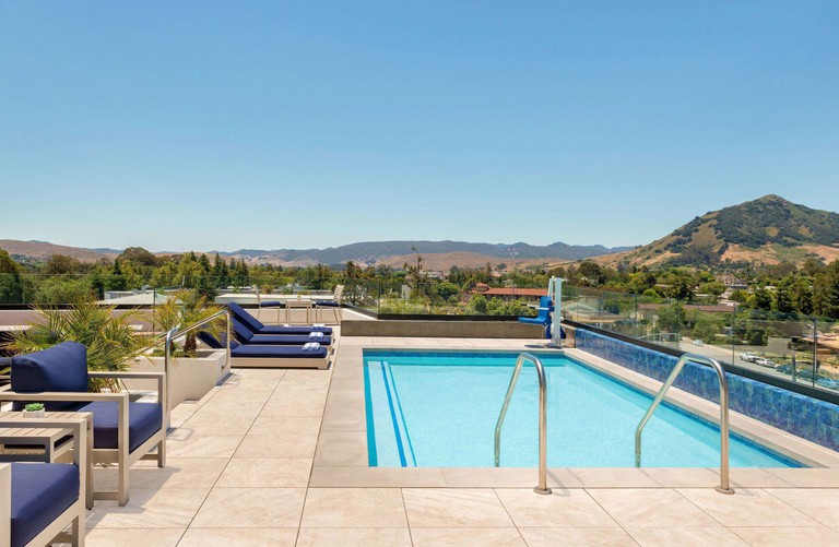 The rooftop pool at La Quinta Inn and Suites, San Luis Obispo, California, is surrounded by blue sun loungers and looks out over the surrounding mountains.