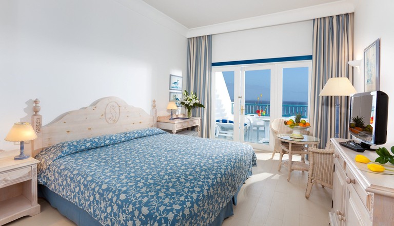 Cosy bedroom with pale wood and rattan furniture, blue accents and ocean-view balcony at Seaside Los Jameos, Lanzarote